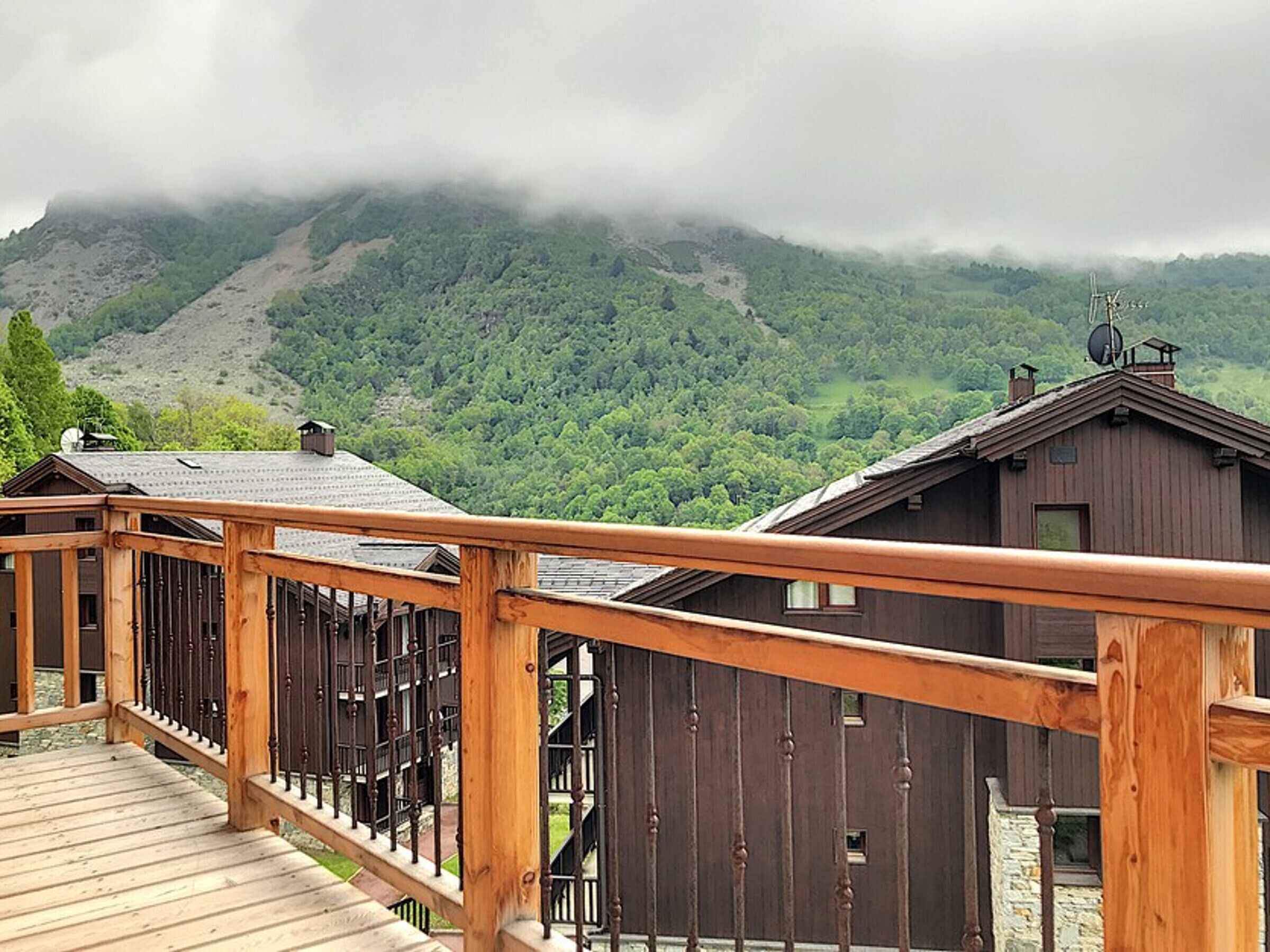 Une terrasse en bois dotée d’une rambarde, qui offre une vue sur un paysage montagneux avec une cabane.