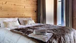 Une chambre à coucher avec une tête de lit en bois, un grand lit recouvert d’une literie blanche, un plaid en fausse fourrure et un coussin sur lequel est inscrit « Case Blanche ».