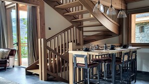Une cuisine moderne avec un escalier en bois, des tabourets de bar et une grande fenêtre donnant sur un mur en pierre.