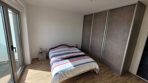 Une chambre à coucher comprenant un lit, une table de chevet, une armoire et une porte-fenêtre coulissante.