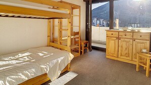 A compact room with a bunk bed, a desk with a chair, and a window with a view of buildings and a mountain. - Ski-in apartment, 2 rooms, 6 ppl, south/west balcony (Les Menuires)