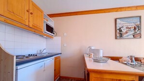 Eine kompakte Küche mit Holzschränken, einer Mikrowelle und einem Herd. Es gibt einen Essbereich mit Tisch und Stühlen sowie ein gerahmtes Bild an der Wand.