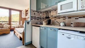 Une cuisine compacte équipée d’un four à micro-ondes, d’une bouilloire et d’une machine à café. Elle comprend également un petit réfrigérateur et un lave-vaisselle. La cuisine est dotée d’un plan de travail carrelé et de meubles de couleur bleu clair.
