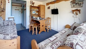 Une pièce chaleureuse avec une table à manger en bois, des chaises, un canapé et un téléviseur fixé au mur.