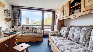 Un salon chaleureux avec un canapé en bois, une table en bois et une vue sur les immeubles par une grande fenêtre.