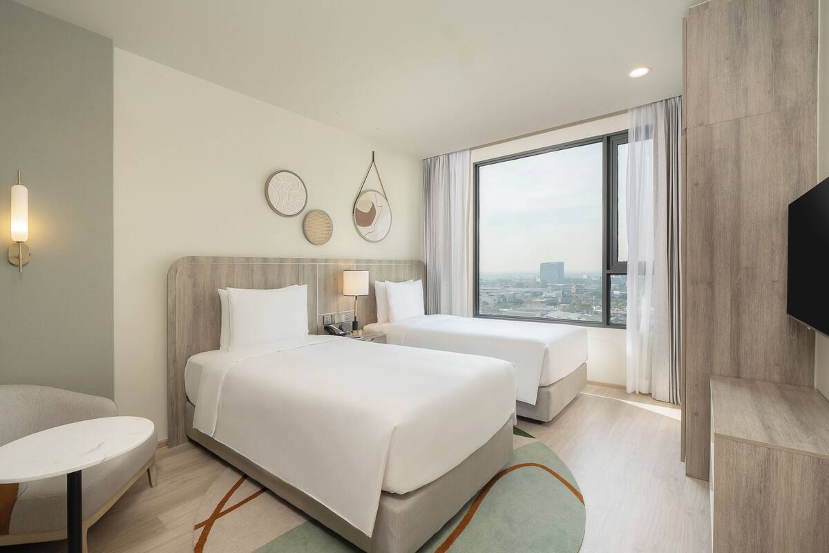 Une chambre d’hôtel avec deux lits, une grande fenêtre donnant sur la ville, un téléviseur à écran plat et une petite table.