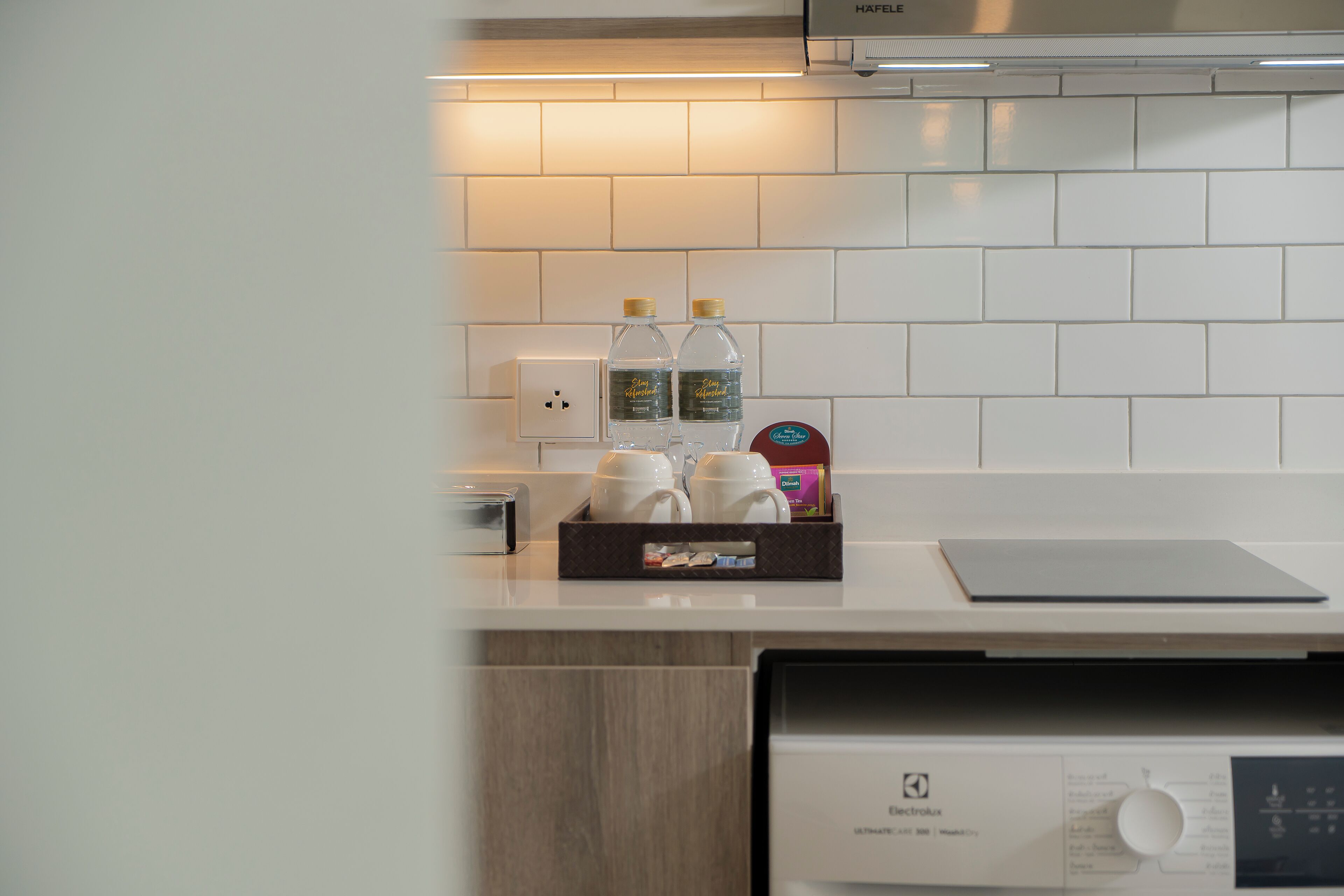 Una cocina con salpicadero de azulejos blancos, una cafetera, dos botellas de agua y una caja de pañuelos.