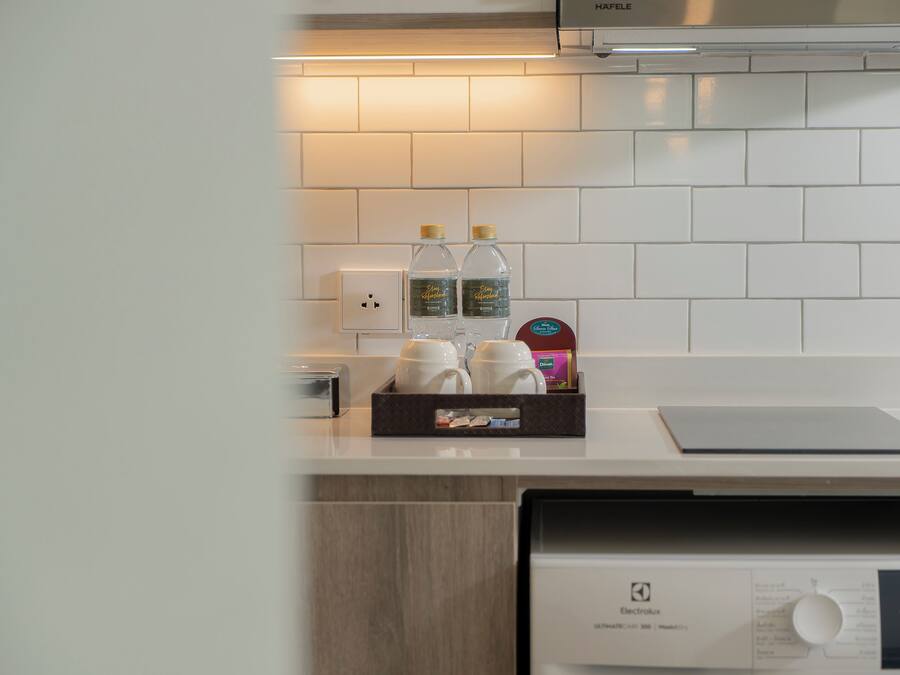 Una cocina con salpicadero de azulejos blancos, una cafetera, dos botellas de agua y una caja de pañuelos.