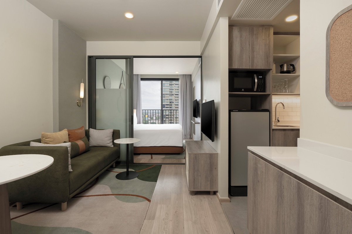 Une chambre d’hôtel moderne équipée d’un canapé, d’une petite table ronde, d’une télévision et d’une kitchenette.