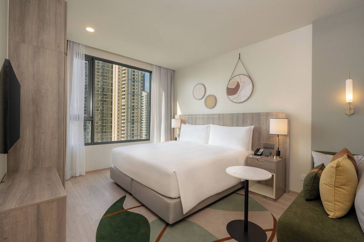 Une chambre d’hôtel moderne dotée d’un grand lit, de tables de chevet, d’un téléviseur à écran plat et offrant une vue sur les gratte-ciel.