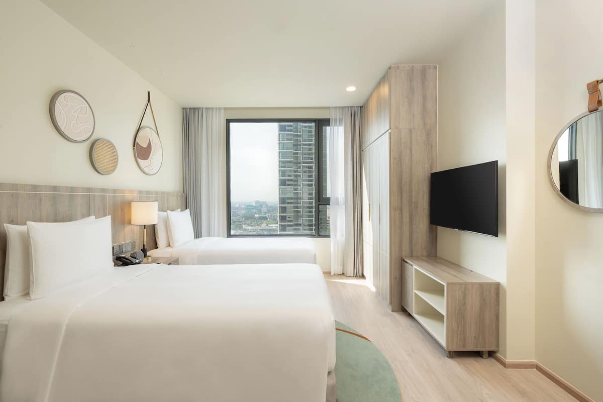 Habitación de hotel con dos camas, televisión y un ventanal con vistas a la ciudad.