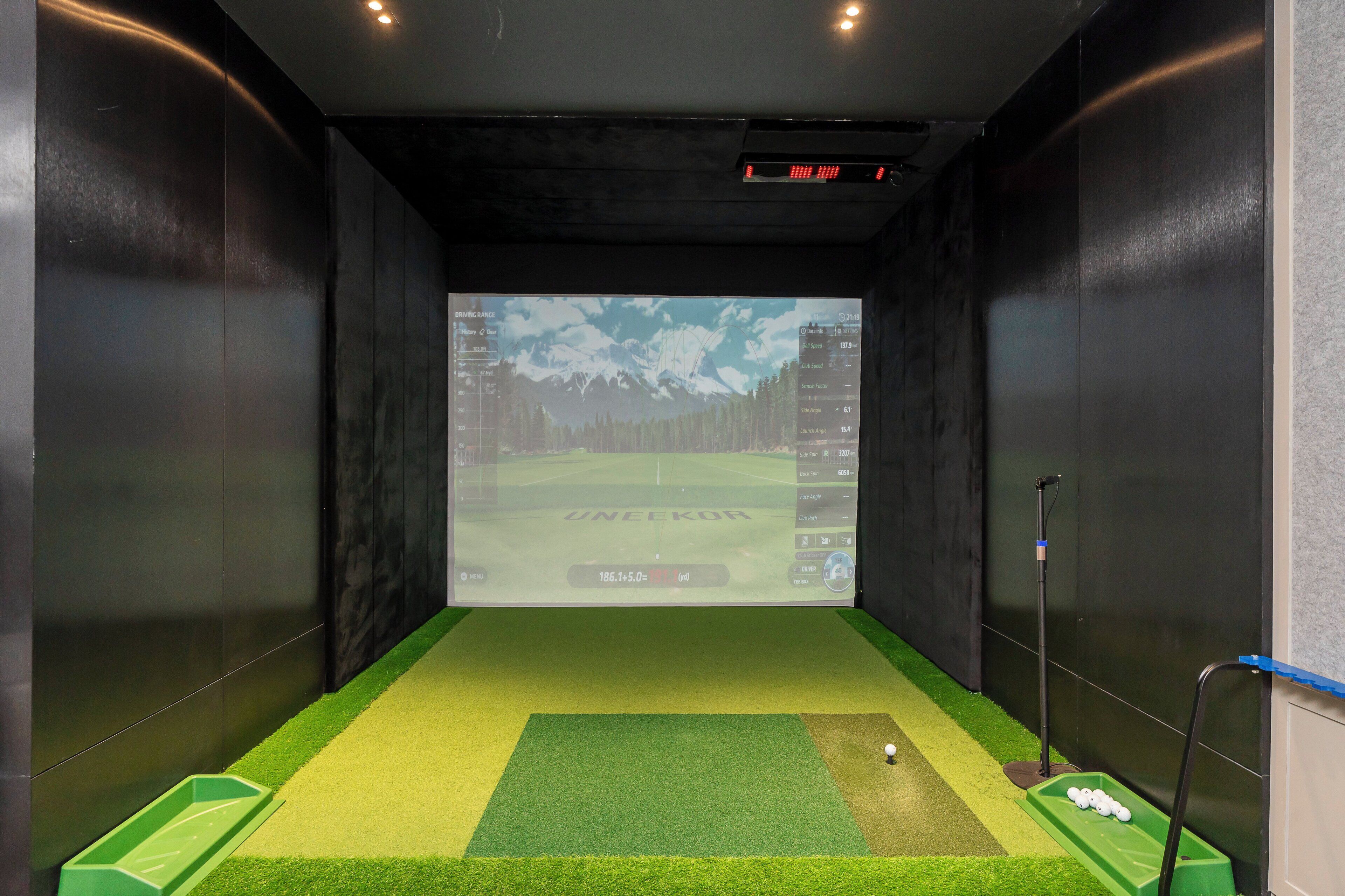 Una sala de simulación de golf con pantalla de proyección, césped artificial y una pelota de golf sobre el tee.