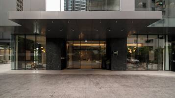 Una entrada de hotel moderna con fachada de vidrio, piso de mármol y zona de acceso cubierta.