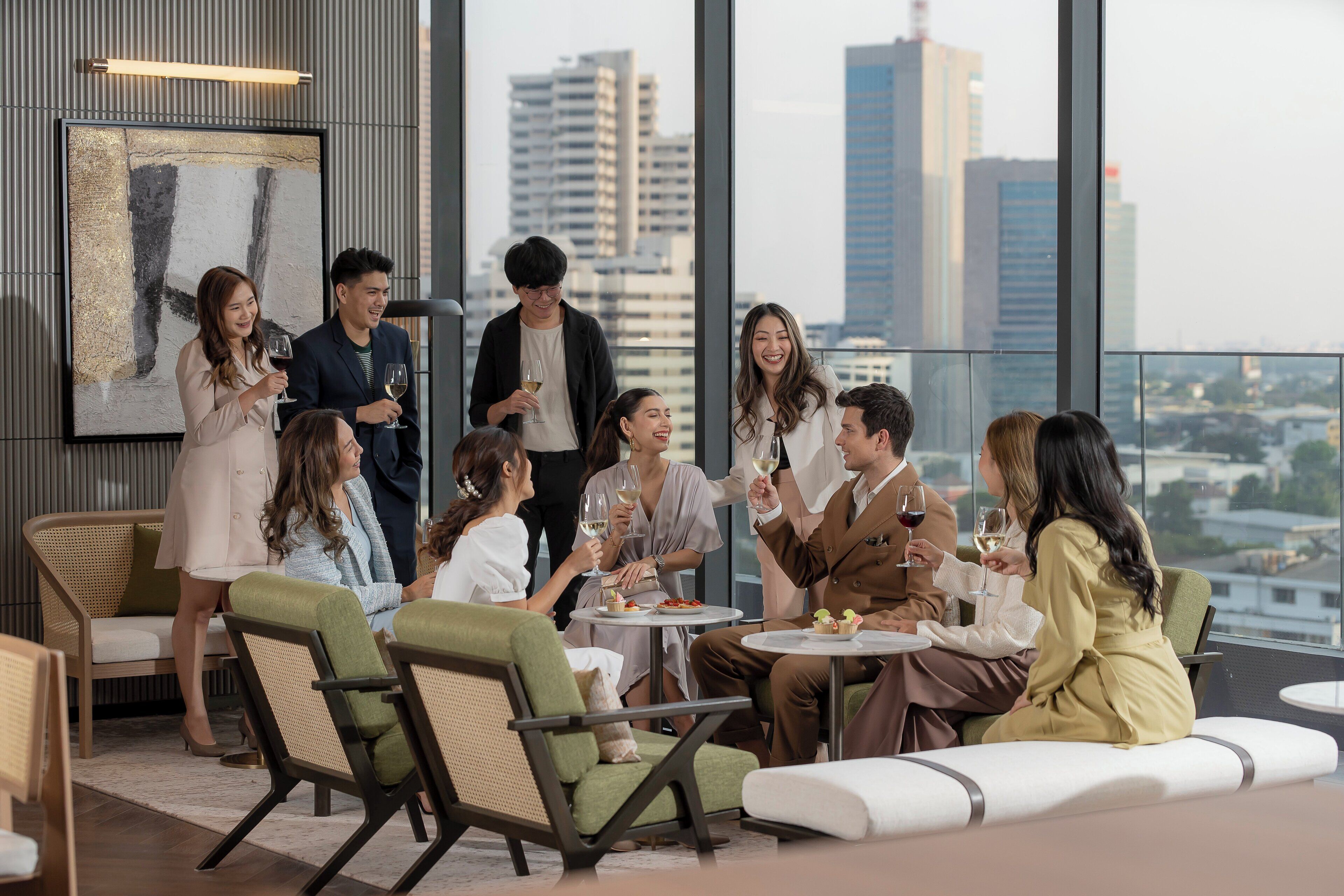 Un grupo de personas sentadas a una mesa con vista a la ciudad, en un espacio interior moderno con techos altos y ventanas amplias.