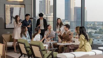 A group of people seated at a table with a city view, in a modern interior with high ceilings and large windows.