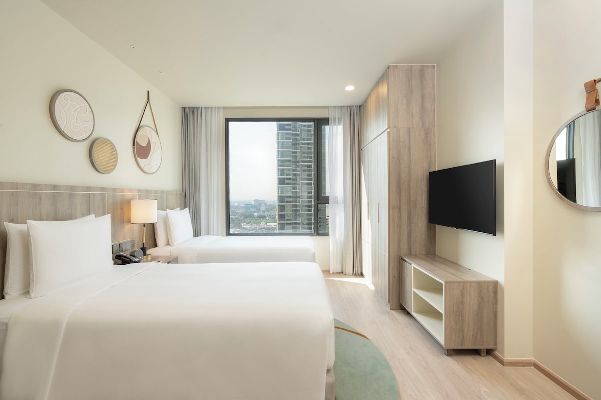 Une chambre d’hôtel avec deux lits, une télévision, un bureau et une vue sur le paysage urbain.