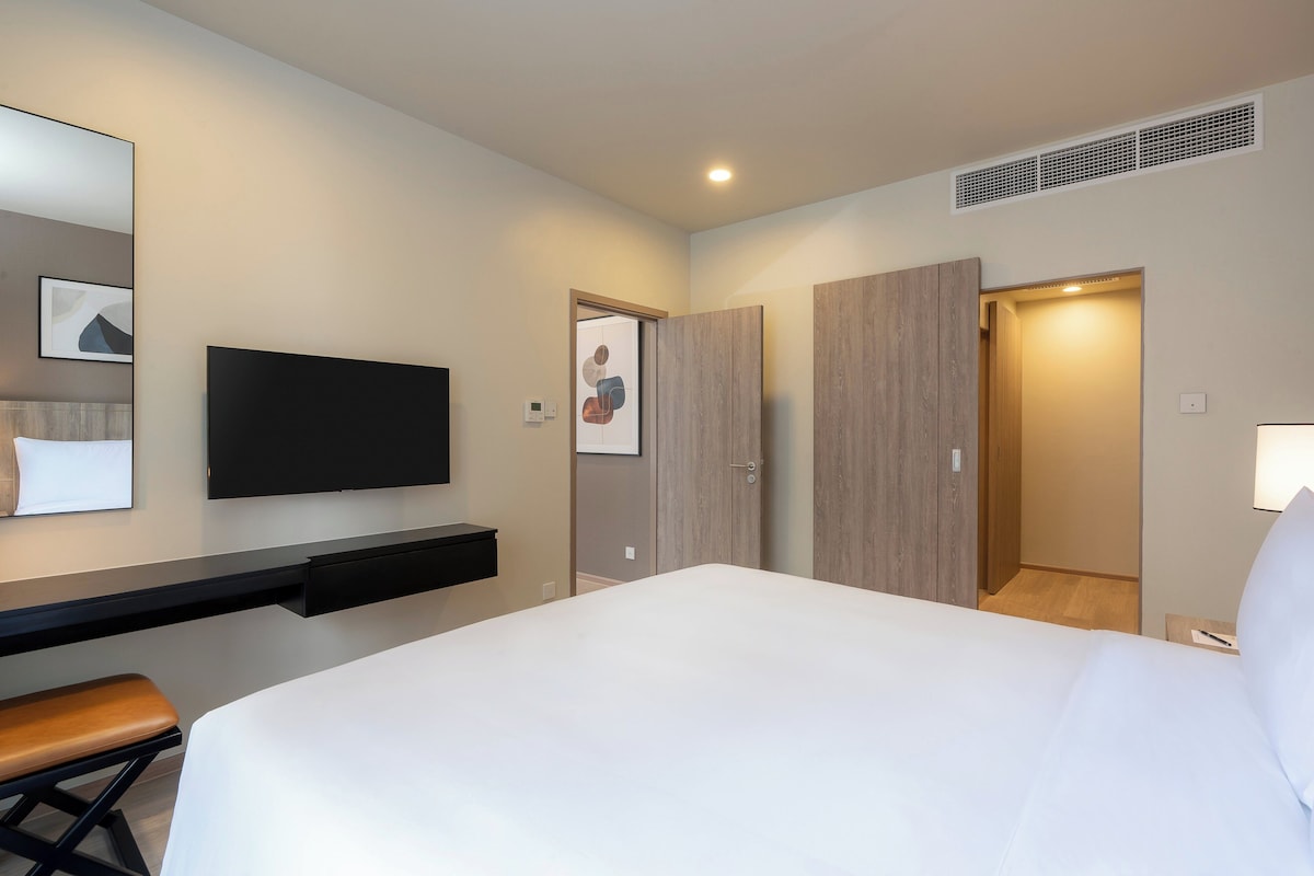 Une chambre d’hôtel moderne dotée d’un grand lit, d’un téléviseur à écran plat fixé au mur, d’un bureau avec une chaise et d’une armoire.