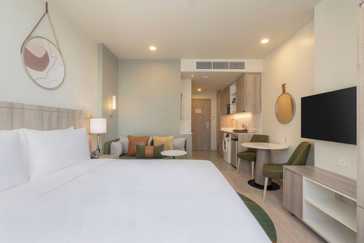 Une chambre d’hôtel avec un grand lit, un canapé, une petite table, une télévision et une kitchenette.