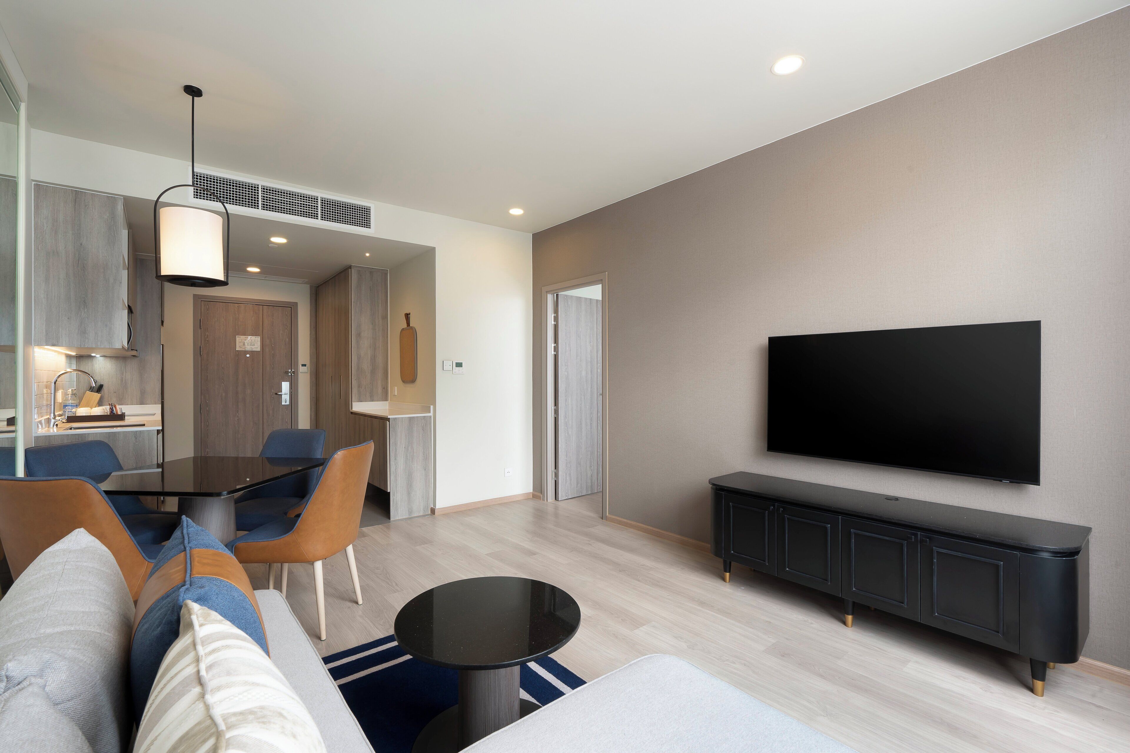 Una sala moderna con televisor de pantalla plana, un comedor con mesa y sillas, y una cocina con estufa integrada.