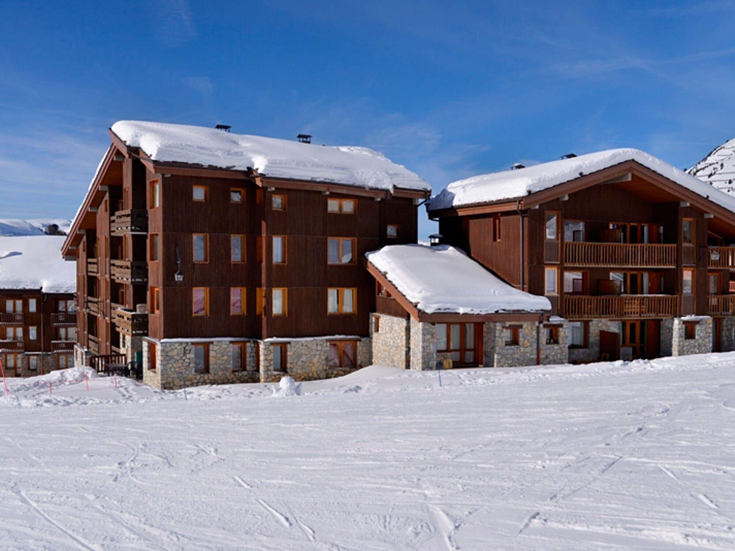 A wooden lodge with multiple balconies and stone foundations, surrounded by snow.