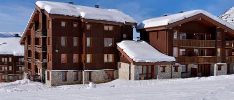 A wooden lodge with multiple balconies and stone foundations, surrounded by snow.