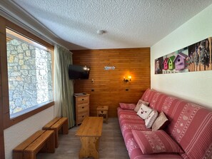 A cozy room with a stone wall, wooden paneling, a television, a sofa, and a wooden table.