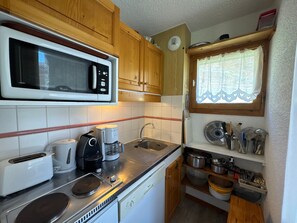 A compact kitchen with wooden cabinets, a microwave, a coffee maker, and a sink.