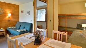 A cozy room with a wooden table, a blue sofa, a bunk bed, and a small window. - Cozy Studio 4 pers · Ski-in · Pets Allowed (Belle Plagne)