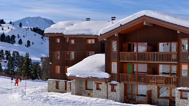 A multi-story wooden lodge with stone accents, a balcony, and a ski slope in the background. - Cozy Studio 4 pers · Ski-in · Pets Allowed (Belle Plagne)