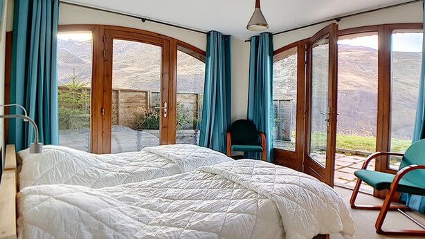 Una camera da letto con un letto grande, una sedia e vista all'esterno tramite ampie finestre.