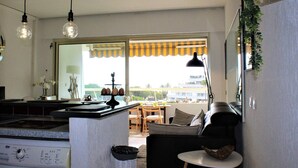 A modern kitchen with a washing machine, a dining area with a table and chairs, and a large window with a view of the outside. - Modern Apartment, Sleeps 4, Air-Conditioned with Parking (Villeneuve-Loubet)