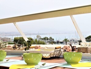 A terrace with a table set for dining, overlooking a marina with boats and a cityscape in the distance. - Modern Apartment, Sleeps 4, Air-Conditioned with Parking (Villeneuve-Loubet)