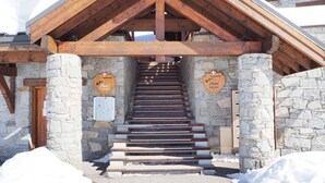 A wooden staircase leading to a stone building with wooden beams. There are two signs on the walls, one reads "Chalet Cembro" and the other "Chalet Epica". - Spacious 4-room apartment, ski-in, balcony, parking (Les Menuires)
