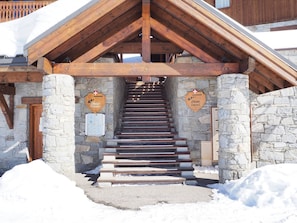 Puinen portaikko johtaa kivirakenteiseen rakennukseen, jossa on puupalkit. Seinillä on kaksi kylttiä, toisessa lukee ”Chalet Cembro” ja toisessa ”Chalet Epica”.
