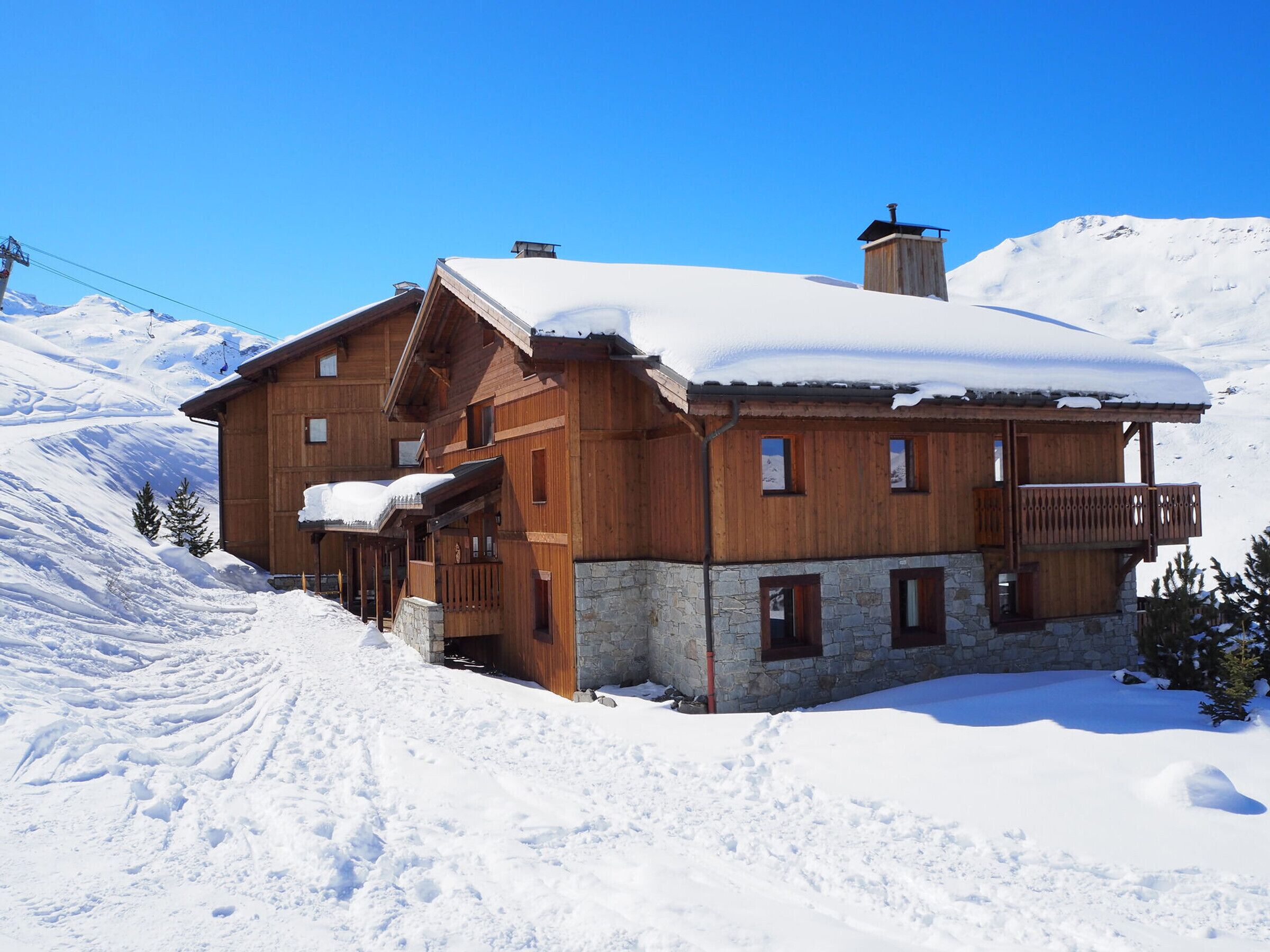 A wooden chalet with a stone foundation, multiple balconies, and a ski lift in the background.