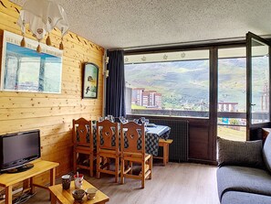 Una habitación acogedora con paredes de madera, una mesa de comedor con sillas, un televisor y un gran ventanal con vistas a un paisaje montañoso.