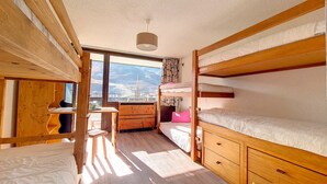 Ein kompakter, gut beleuchteter Raum mit Etagenbetten, einem Holztisch und einem Fenster mit Blick auf die Berge.