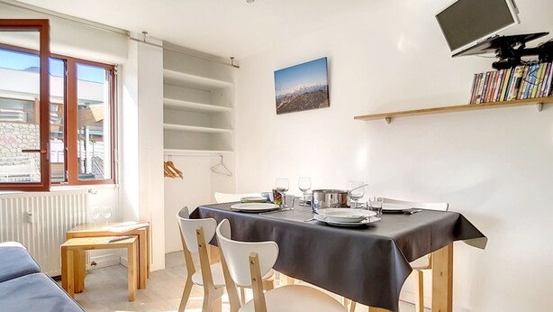 Een eetruimte met een tafel voor vier personen, een aan de muur bevestigde televisie en een boekenkast met boeken.