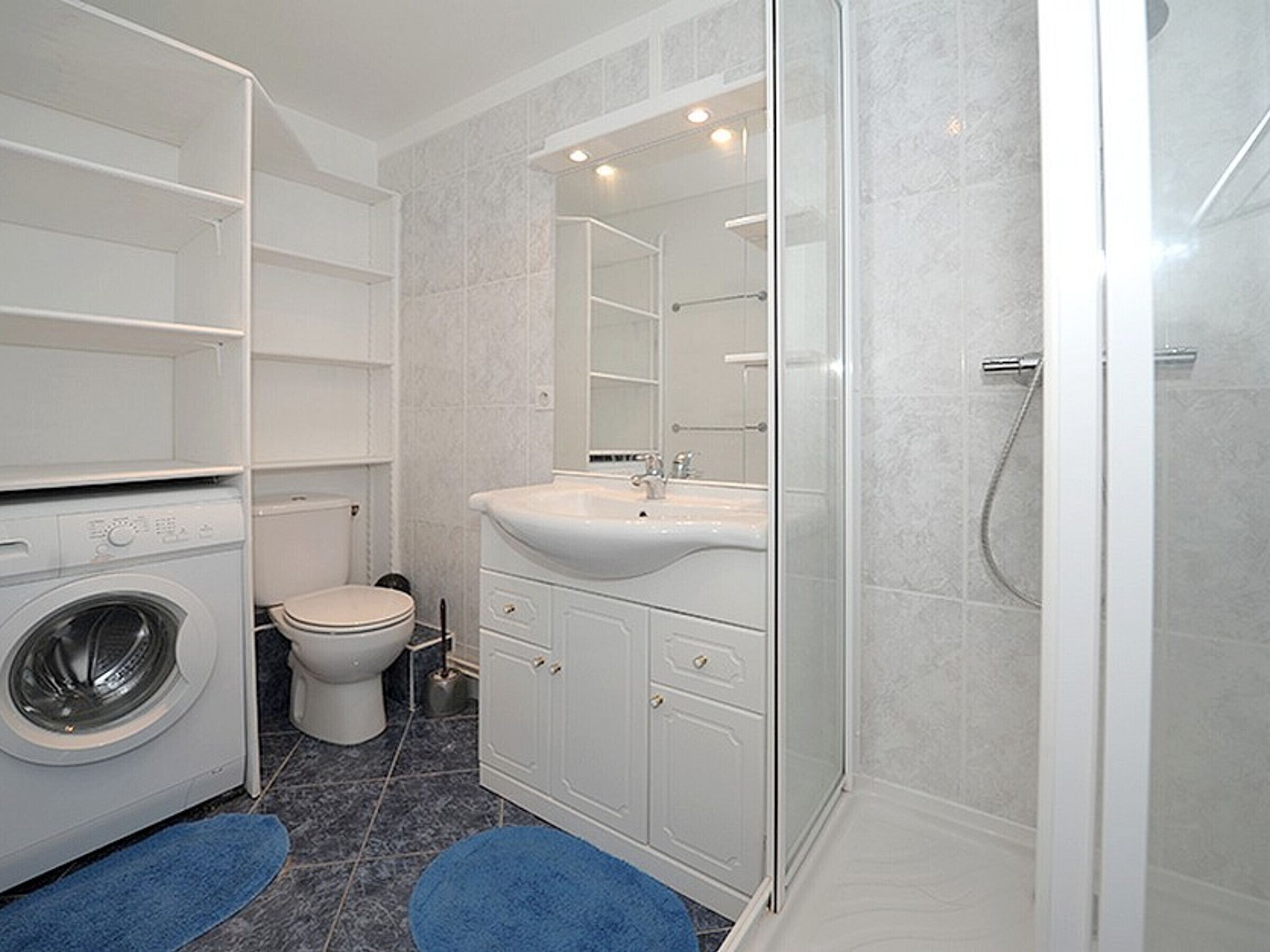 Une salle de bain moderne équipée d’un lave-linge, de toilettes, d’un lavabo et d’une douche.