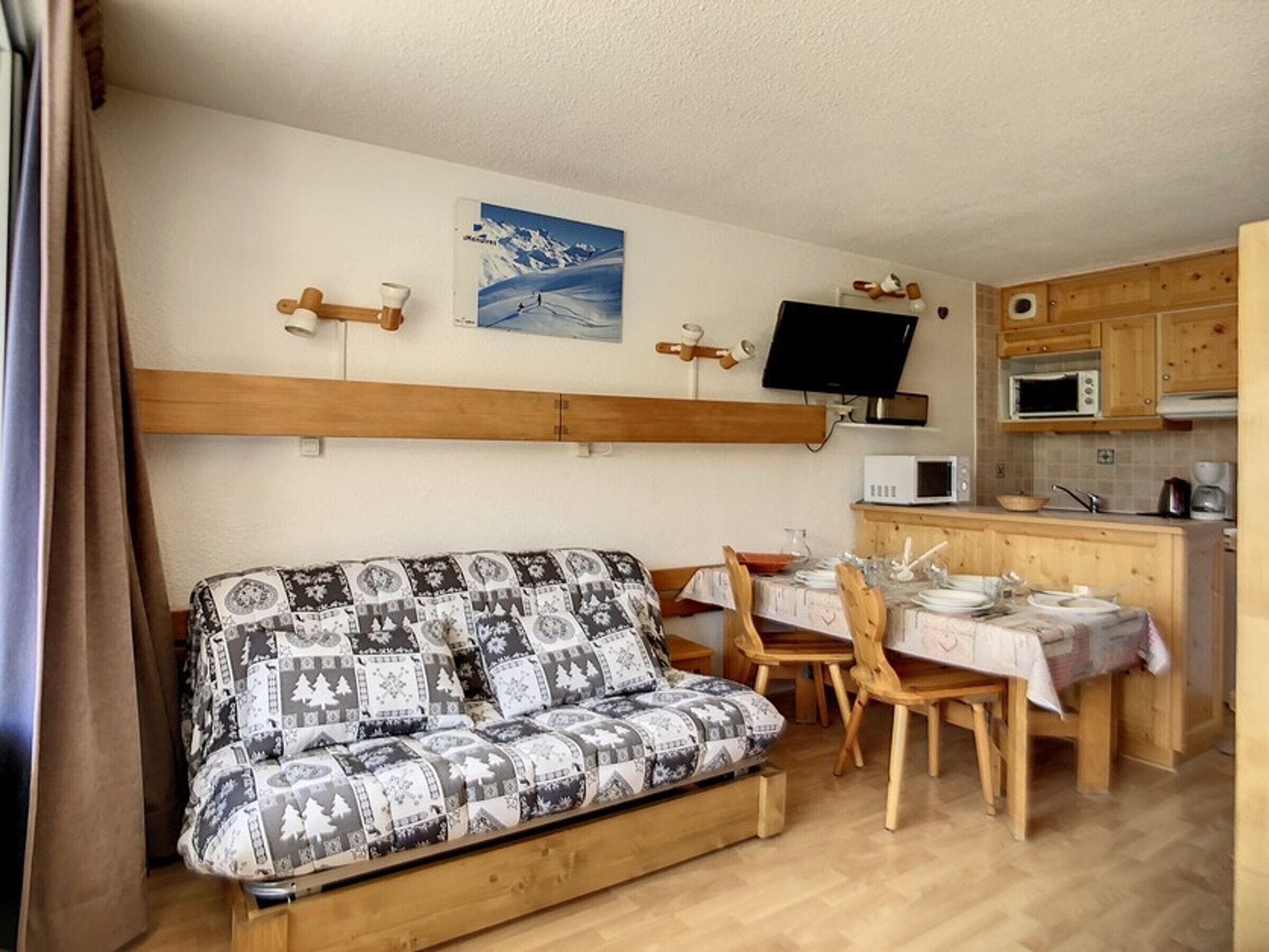 Een gezellig interieur van een chalet met een bank, eettafel, stoelen, een televisie en een keukenhoek.