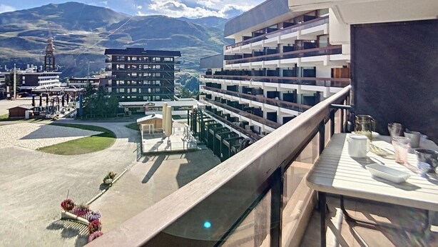 Varanda de hotel com vista para uma paisagem montanhosa, uma área de estacionamento e um edifício com vários andares.