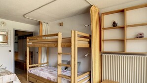 Quarto com beliche, piso de madeira, uma mesinha e um radiador.