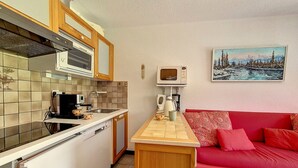 A compact kitchen with a microwave, coffee maker, and toaster. A red sofa with patterned cushions is in the living area.