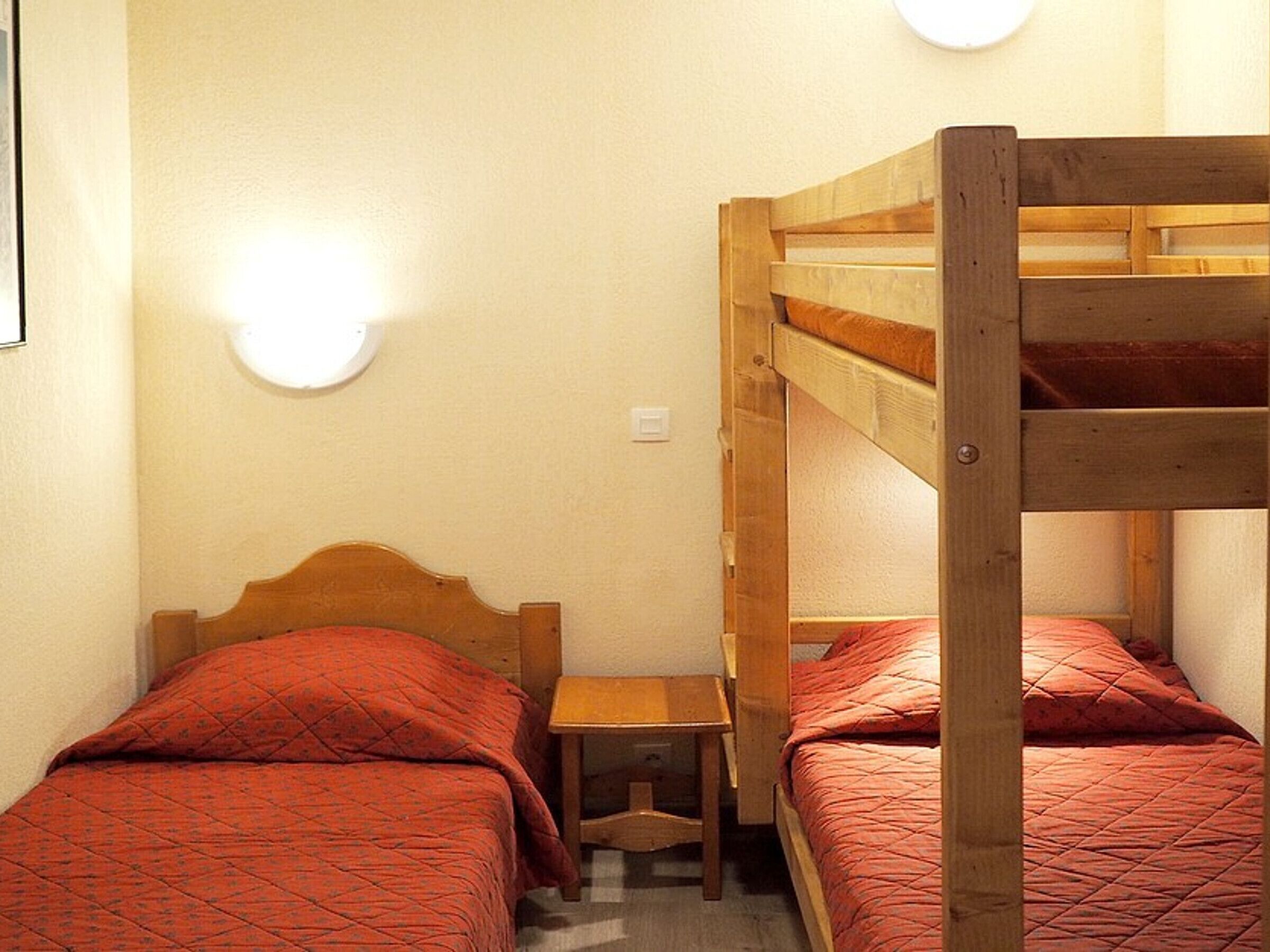 A bunk bed room with two beds, a small wooden table, and a wall-mounted light fixture.