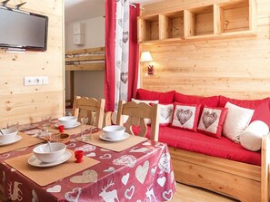A cozy room with a wooden interior, a dining table set with white plates and bowls, a red sofa with heart-patterned cushions, and a television mounted on the wall. - Cozy apartment with terrace - Ski-in/ski-out (Les Menuires)