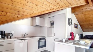 Ett kompakt kök med vita skåp, en inbyggd ugn, en mikrovågsugn och en plats för kaffebryggaren.