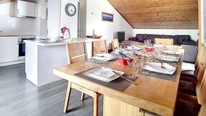 Ett modernt kök med vita skåp, ett träbord med plats för sex personer och ett mysigt vardagsrum med en soffa och en tv.
