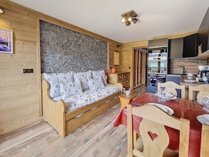 A cozy cabin interior with a wooden sofa, a dining table set for two, and a kitchen area.