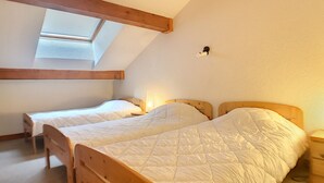 Quarto com duas camas de madeira, um claraboia e uma pequena mesa de cabeceira com abajur.