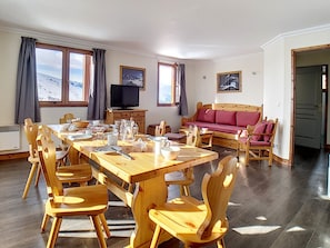 A spacious room with a wooden dining table, chairs, a sofa, and a television.